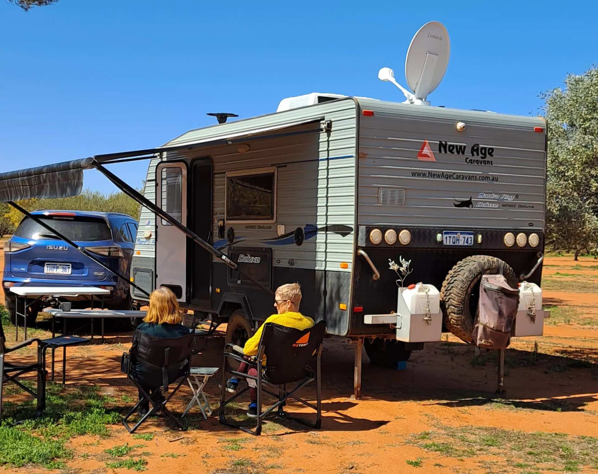 A photo of a camper van with two elderly people sitting in front of it.